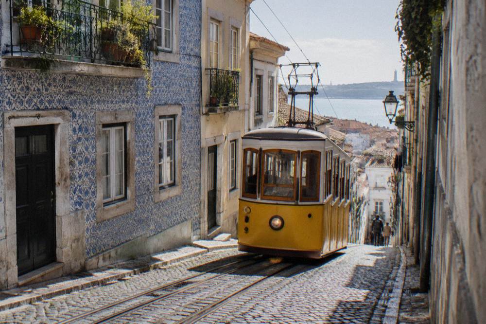 A yellow tram climbs a steep cobbled street between tiled facades with the river visible in the distance.