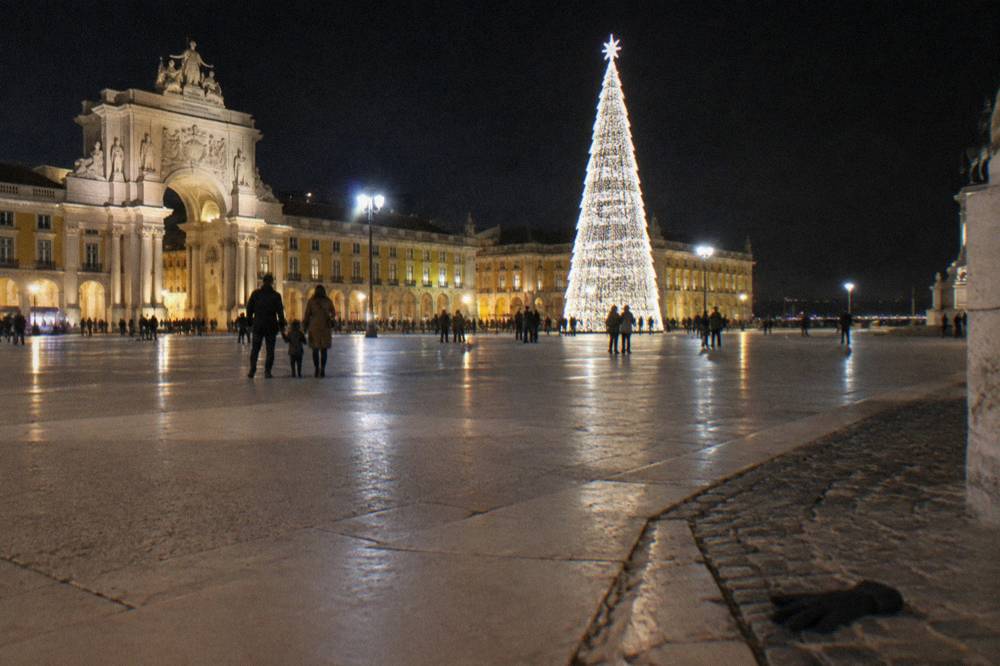 Night view of Praça do Comércio with a tall lit Christmas tree, glowing arcades, scattered people, and a glove near the curb.